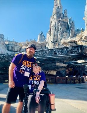 wheelchairs | SMA News Today | Tyler and Dara Bailey pose in front of what looks like a Star Wars section of Disneyland, or similar. Both are wearing purple Cure SMA T-shirts