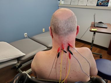 A man is shown with electrodes placed on the back of his neck and upper back. 