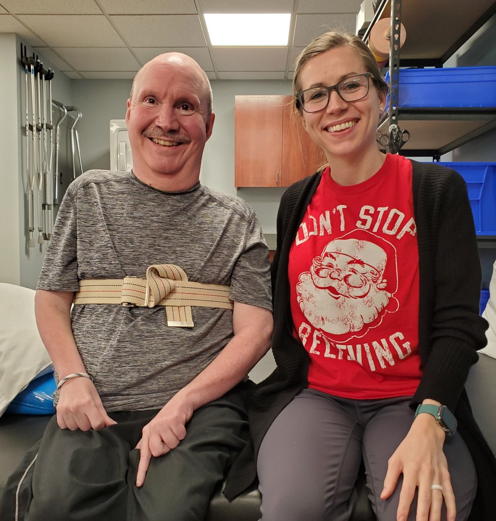 A man and woman sit on a bench together in a physical therapist's office.