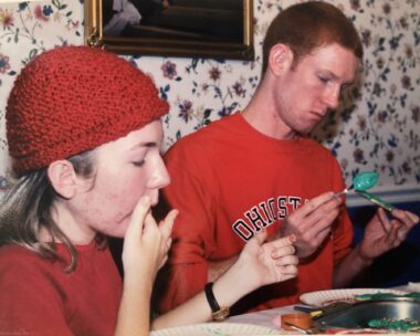 A teenage boy and girl are shown sitting at a table in a dining room, decorating cookies.