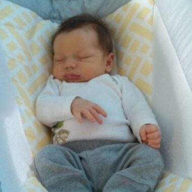 A baby sleeps in some sort of chair or swing.