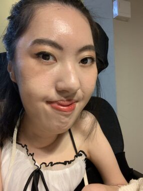 A woman in her 20s smiles for a closeup photo. She's wearing a white and black spaghetti-strap dress. Her brows are thicker than usual. 