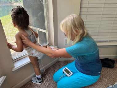 A physical therapist attaches electrode pads to a young girl for NISE-Stim therapy.