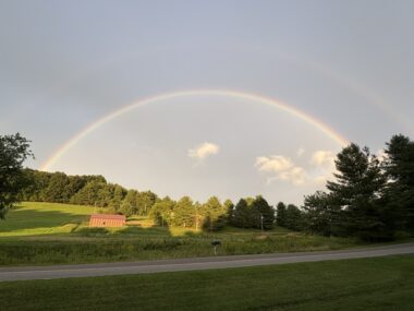 A double rainbow appears in the sky above green rolling hills.